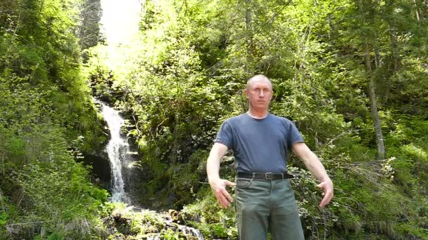 Al rallentatore. L'uomo medita vicino alla cascata, mani in alto. Cambiamento di obiettivo — Video Stock