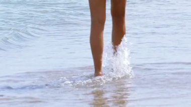 Ağır çekim. Kadın bacaklar dalgalar arasında yaz deniz kıyısında gitmek