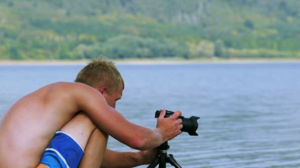 4K. Fotógrafo Guy ajusta câmera na margem do lago — Vídeo de Stock