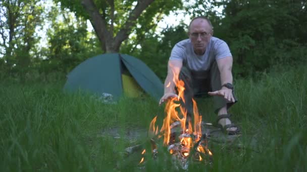 Velho Turista Aquece Mãos Perto Tenda Camping Com Fogo Movimento — Vídeo de Stock