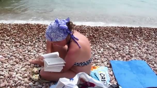 Γυναίκα στο μαντήλι διαβάζει το βιβλίο σε μια παραλία — Αρχείο Βίντεο