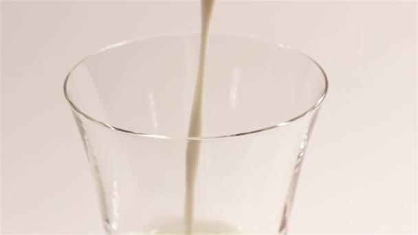 Milch fließt in transparenter Tasse auf weißem Hintergrund — Stockvideo