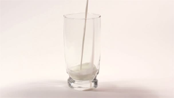 Γάλα ρέει σε διαφανές φλιτζάνι σε άσπρο φόντο — Αρχείο Βίντεο