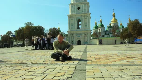 Печальный человек сидит на тротуаре напротив церкви. Временной интервал — стоковое видео
