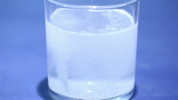 Таблетка блестящего аспирина в стекле на синем фоне — стоковое видео
