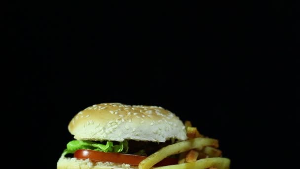 Hamburger met gebakken aardappel in rotatie op zwarte achtergrond — Stockvideo