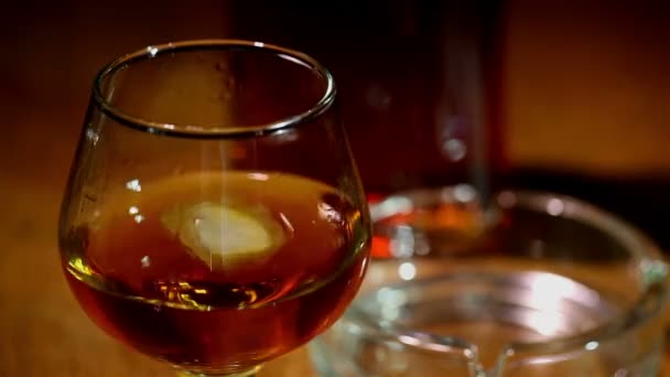 Isen faller i ett glas med cognac, whisky på nära håll — Stockvideo