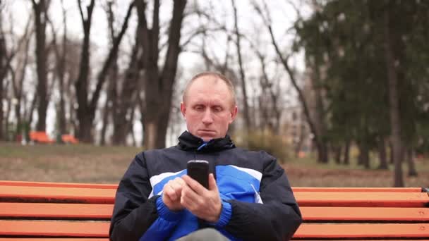 Volwassen ernstige man praten op mobiele in park. Vooraanzicht — Stockvideo