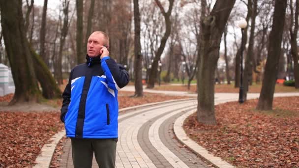 Felnőtt ember beszél a mobil őszi parkban — Stock videók