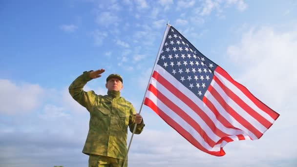 Soldado saludo con bandera americana contra el cielo azul. Escena de cámara lenta — Vídeo de stock