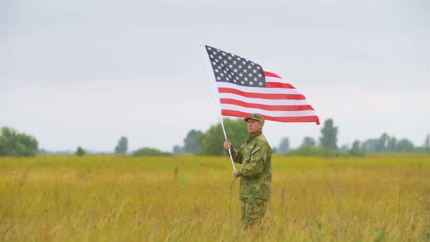 Soldado caminando en el campo con bandera americana. Escena de cámara lenta — Vídeo de stock