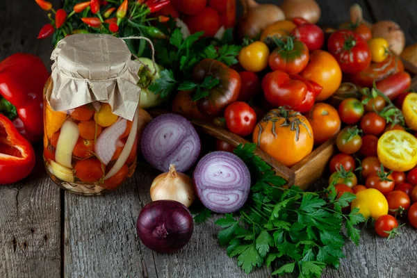 Tomatoes, peppers, onions on the table. Preservation of the autumn harvest of vegetables. Glass jar with pickled tomatoes. Wooden background. Vegetable food. Tomato of different varieties.