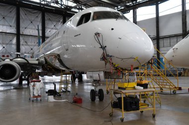 Ukraine, Kyiv - November 25, 2020: The Embraer E190LR UR-EMD aircraft is in the hangar for technical repair and maintenance. Aircraft diagnostics, storage, service. Plane. Ladders for mechanics clipart