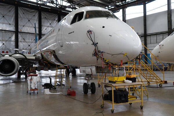 Ukraine, Kyiv - November 25, 2020: The Embraer E190LR UR-EMD aircraft is in the hangar for technical repair and maintenance. Aircraft diagnostics, storage, service. Plane. Ladders for mechanics