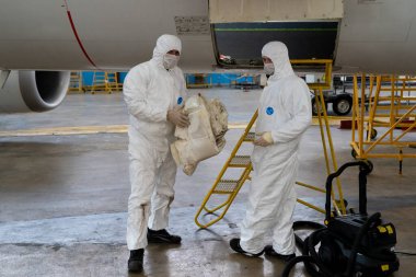 Ukrayna, Kyiv - 25 Kasım 2020: İşçiler karantina ve salgın sırasında tıbbi maske ve koruyucu giysiler ile çalışıyorlar. Çalışan tamirciler uçağı tamir ediyor. Uçak motoru tamiri. Hangar