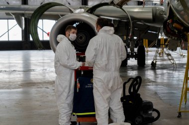 Ukrayna, Kyiv - 25 Kasım 2020: İşçiler karantina ve salgın sırasında tıbbi maske ve koruyucu giysiler ile çalışıyorlar. Çalışan tamirciler uçağı tamir ediyor. Uçak motoru tamiri. Hangar
