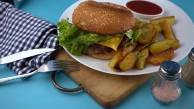 Köy patatesli hamburger menüsü. Patates ve salatalı ev yapımı kusurlu hamburger. Masada beyaz bir tabakta, tahta bir tahtanın üzerinde yemek var. Kızarmış çörek..