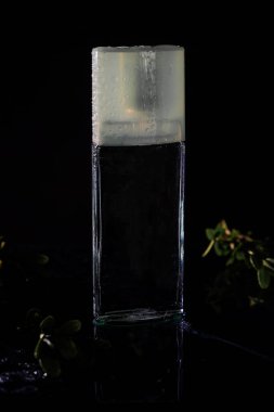 Siyah arka planda parfüm şişesi. Tuvalet suyu şişesi, su serpintisi ve mesaj için yer. Etiketsiz ambalaj. Parfüm Spreyi.
