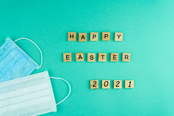 Happy Easter 2021 Medical masks. The phrase is laid out in wooden letters. View from above. Motivation. Medical masks. Mask. Copy space. Postcard for doctors.