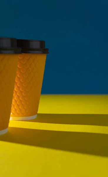 Yellow ribbed paper cup with plastic lid for takeaway beverage in fast food restaurants. A cup of coffee, cocoa, tea from a street cafe. Place for your text. Blue background.