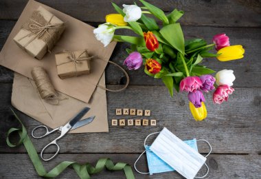 Paskalyanız kutlu olsun. Tatil için hediye paketi. Ahşap arka planda bir buket lale. Tıbbi maskeler. Hediye ve paket kağıdı. Üst görünüm maskesi.