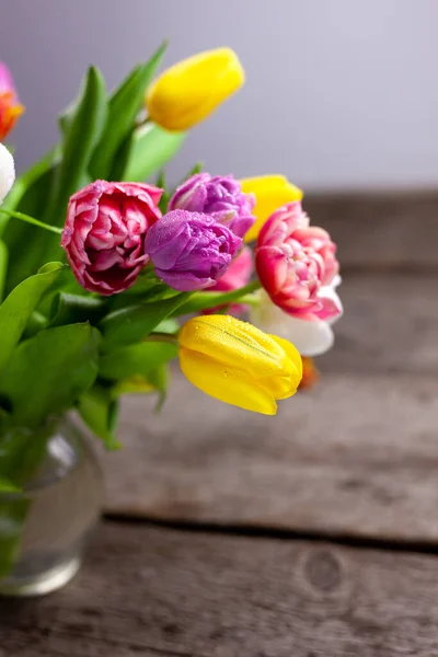 Vase with multi-colored bouquets of tulips on a wooden table. Tulip with dew drops. Selective focus. Copy space. Spring background