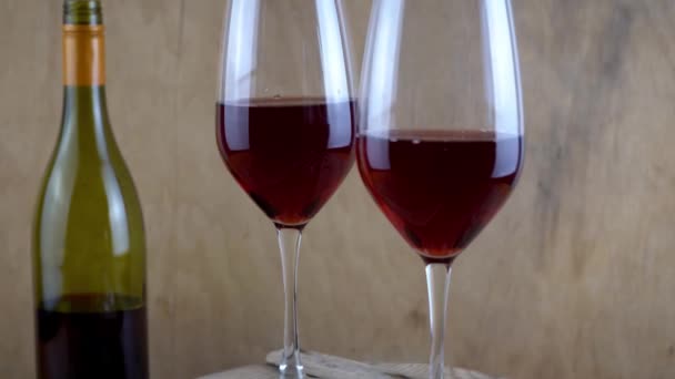 Deux verres de vin rouge. Boisson alcoolisée dans un verre. Une bouteille de vin. Fond en bois. — Video