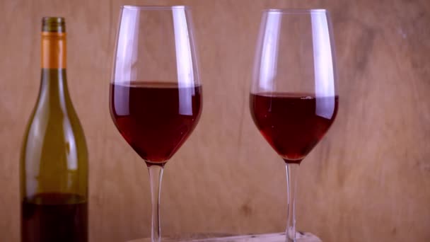 Deux verres de vin rouge. Boisson alcoolisée dans un verre. Une bouteille de vin. Fond en bois. — Video