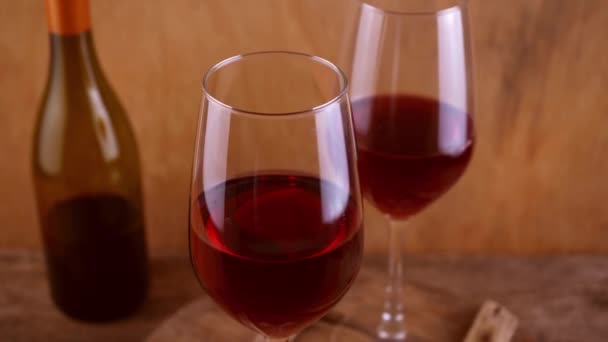 Dos copas de vino tinto. Bebida alcohólica en un vaso. Una botella de vino. Fondo de madera. — Vídeo de stock