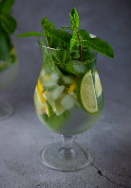 Naneli limon ferahlatıcı kokteyl mojito rom ve buzlu gri arka planda cam. Koyu taş masada mojito kokteyli. İçkiler için cam gibi bir bardak. Barda limonata. Klasik içki..