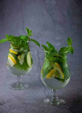 Naneli limon ferahlatıcı kokteyl mojito rom ve buzlu gri arka planda cam. Koyu taş masada mojito kokteyli. İçkiler için cam gibi bir bardak. Barda limonata. Klasik içki..
