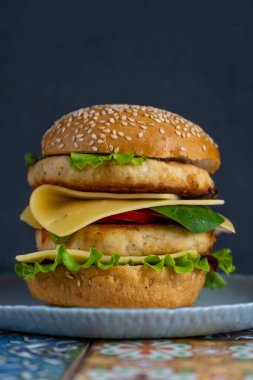 Hamburger ekmeği, peynirli duble tavuk pirzolası, marul, roka ve turp. Et, sebze ve ekmek. Malzemeler. Tabakta ev yapımı burger. Renkli kiremitlerden yapılmış tablo.