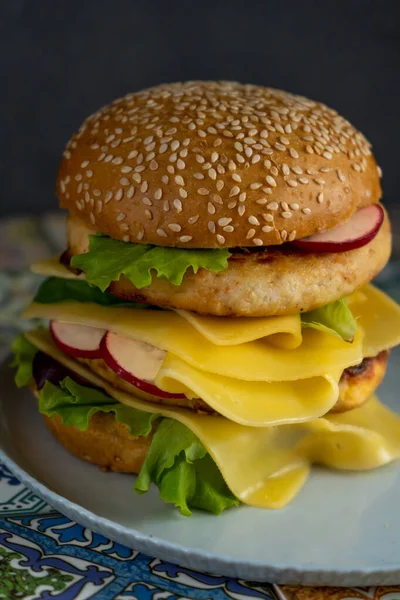 Pan de hamburguesa, doble chuleta de pollo con queso, lechuga, rúcula y rábano. Carne, verduras y pan. Ingredientes. Hamburguesa casera en un plato. Mesa hecha de azulejos de colores —  Fotos de Stock