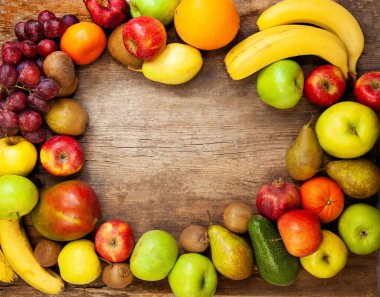 Ahşap bir arka planda çok renkli meyvelerin çerçevesi. Meyve topla. Muz, elma ve armut. Limon, mango, avokado ve üzüm. Meyve yaz geçmişi. Boşluğu kopyala.
