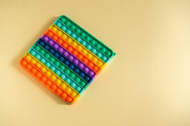 Büyük popit sarı arka planda izole edilmiş. Parlak silikon çizgili oyuncak. Büyük Patlama. Yakın plan. Çocuklar için Popit. Gökkuşağı, parmaklarıyla kabarcıklara bastırıyor. Çocuklar için yeni bir anti-stres oyuncağı. Boşluğu kopyala.