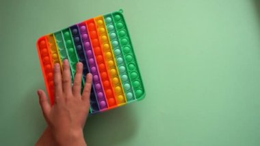 Parlak silikon çizgili oyuncak Big Pop It. Çocuk gökkuşağıyla oynuyor, parmaklarıyla baloncuklara bastırıyor, üst görüntü yakın çekim. Çocuklar ve yetişkinler için yeni bir anti-stres oyuncağı. Popit oyuncusuyum. Kare şekil