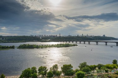 Kyiv 'in sağ yakasının panoramik manzarası. Dinyeper nehri, akşam ve gün batımı. Metro köprüsü. Görüş. Balkondan manzara güzel. Güzel bulutlu gökyüzü. Ukrayna. Kumsalı olan bir baraj..