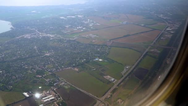 玄関の土地だ。飛行機の窓から地面の眺め。上から多色のフィールド。乗客席の旅客機内での飛行。旅行だ。着陸. — ストック動画