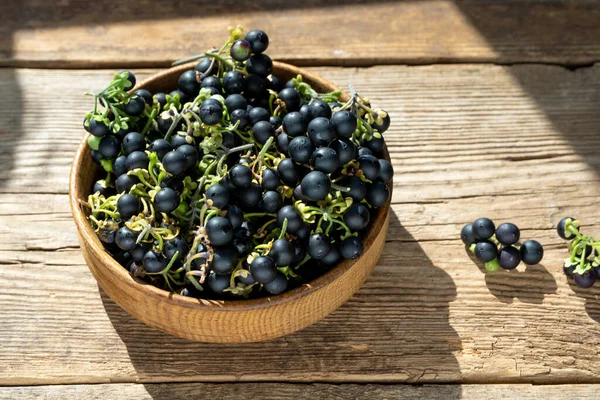 Masanın üzerinde bir tabakta siyah itüzümü. Yemek pişirmede İtüzümü. Sağlıklı yiyecekler. Pişirmek için hasat.