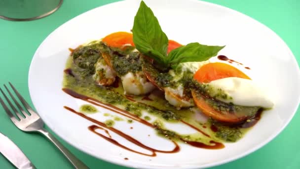 Caprese salad with tomatoes, mozzarella and basil. Red and orange tomatoes with white cheese and sauce. Portion of food on a plate in a restaurant. View from above. Delicious healthy food — Stock Video
