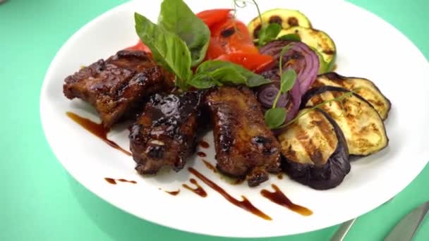 Carnes y verduras a la parrilla. Calabacín, pimientos, cebolla roja y albahaca. Medallones de cerdo frito. Comida en un plato blanco en un restaurante. — Vídeos de Stock