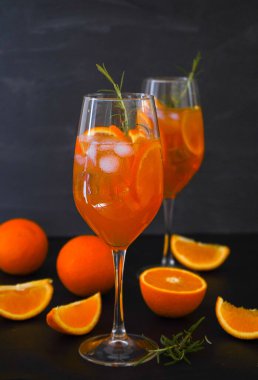 Aperol spritz, aperol, Prosecco, soda ve portakal dilimli bir bardakta servis edilen yaz içkisidir. Şarap kadehinde buzlu kokteyl ve barda biberiye. Siyah arka plan. İçkileri tazeleme konsepti. Aperatif.