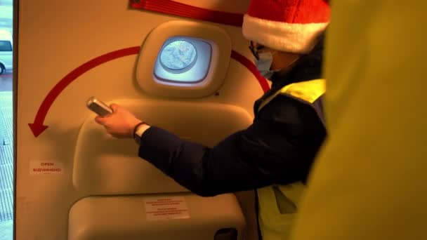 Kiev, Ucraina - 29 dicembre 2020: Una hostess con una maschera medica apre la porta di un aereo Boeing. La ragazza col cappello di Babbo Natale. Porta dell'aereo, entrata dopo l'atterraggio. L'aereo dall'interno — Video Stock