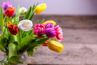 Ahşap bir masanın üzerinde çok renkli lale buketleri olan bir vazo. Çiğ taneli lale. Seçici odaklanma. Uzayı kopyala Bahar arka planı. Çiğ taneli laleler.