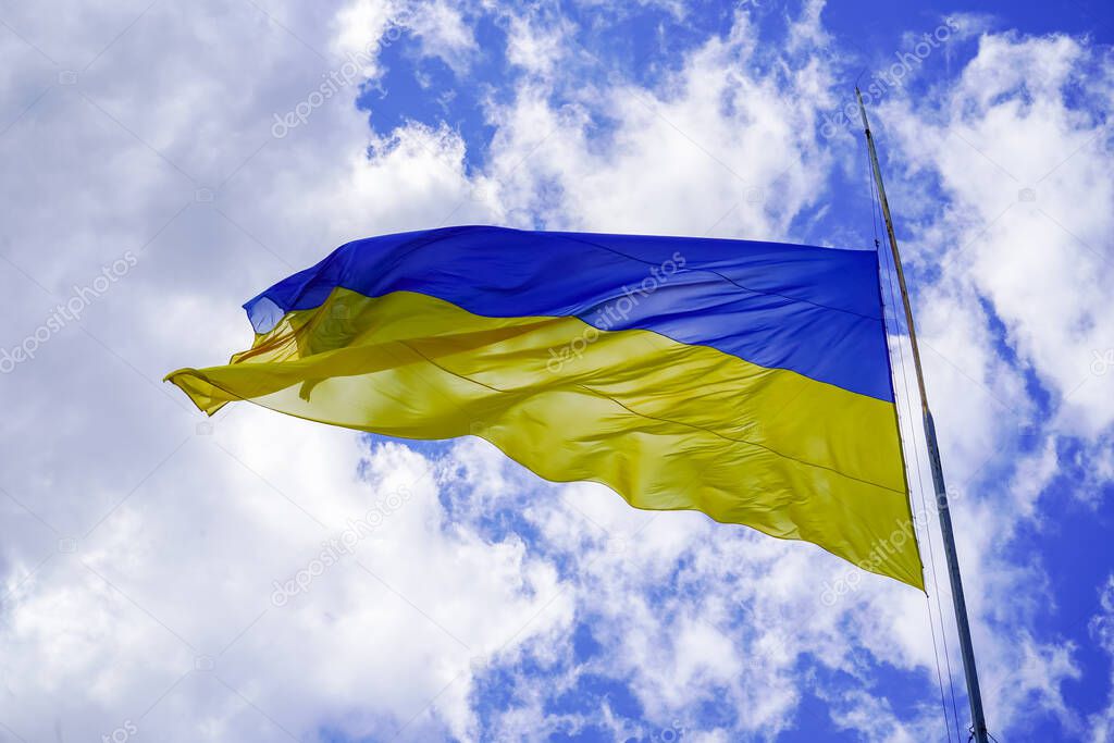 The yellow-blue flag of Ukraine flutters against the blue sky. Ukrainian symbol. A large flag on a flagpole flutters in the wind.