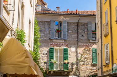 Pencereler çok renkli ve panjurlu. İtalya yaz günü dar ve boş bir cadde. İtalyan tarzı ön cephe mimarisi. Como 'daki ev duvarı.