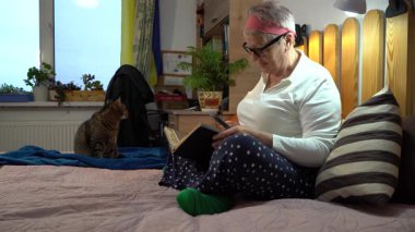 Büyüteçle bak. Yaşlı bir kadın yatakta oturmuş posta pullarından oluşan bir albüme bakıyor. Büyükanne ve hobisi evde.