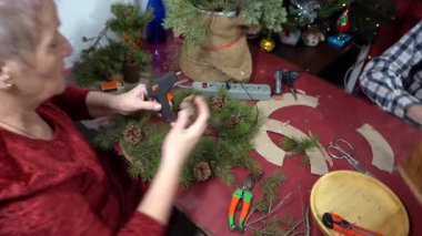 Büyükannem Noel ağacı çelengi yapıyor. Yaşlı kadın çam dallarını süslüyor. Yapıştırıcı kozalakları. Zanaat
