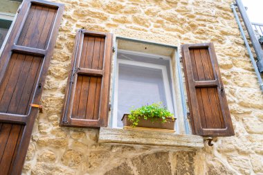 Wooden shutters on the window of an old house in San Marino. A pot of flowers on the windowsill. Stones wall