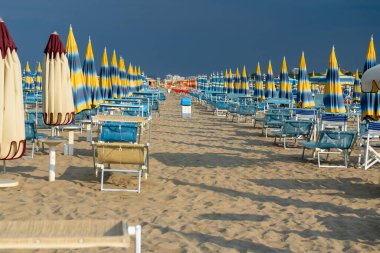 Şemsiyelerle kumlu sahilde güneşleniyorlar. Boş sahil beldesi. Sahil şeridi şezlongunda güneş banyosu. Yazın mavi yağmurlu gökyüzü